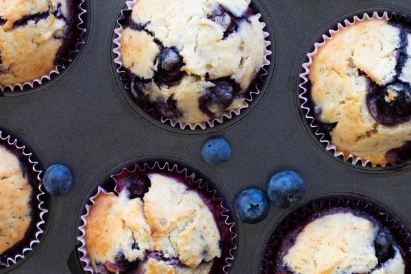 Blueberry Banana Muffins on a muffin baking tray with fresh blueberries.
