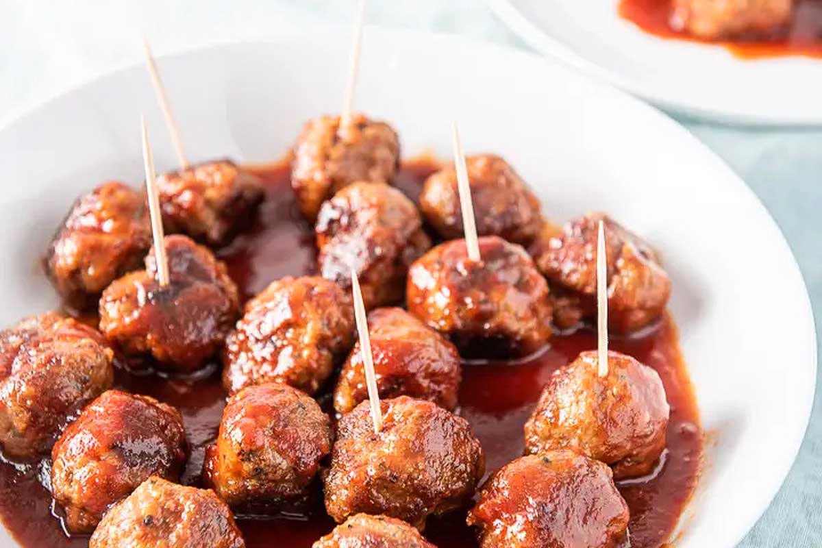 Meatballs in bourbon sauce in a white serving bowl.