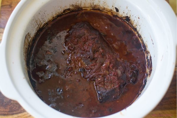 White slow cooker pot filled with brisket with red wine and onions.