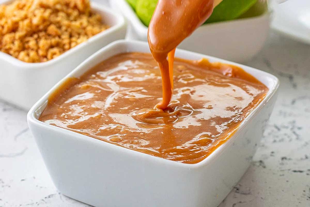 Caramel dip in a white bowl dripping from spoon.