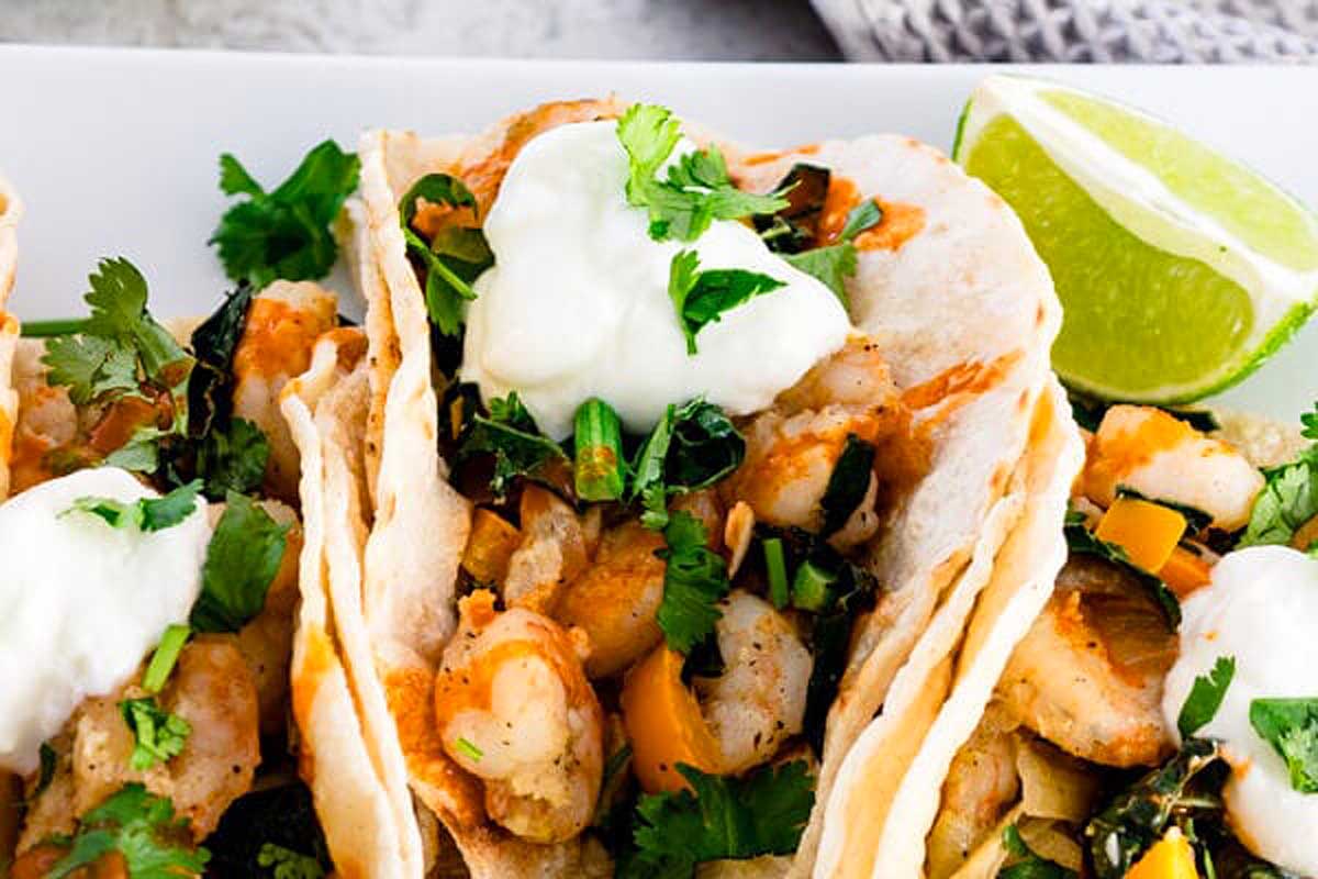 Shrimp tacos with sour cream and lime on a white plate.