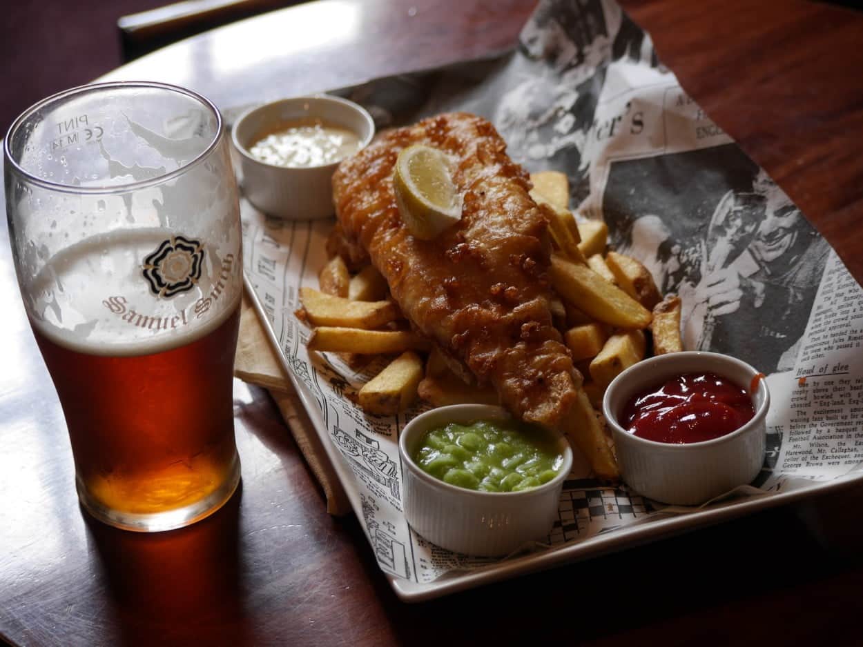England’s Fish and Chips on a plate lined with newspaper next to a beer.