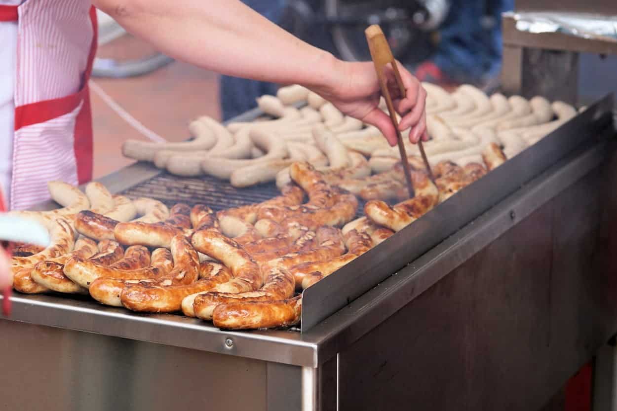 Bratwurst on an outdoor grill in Germany with a man's hand turning the sausages.
