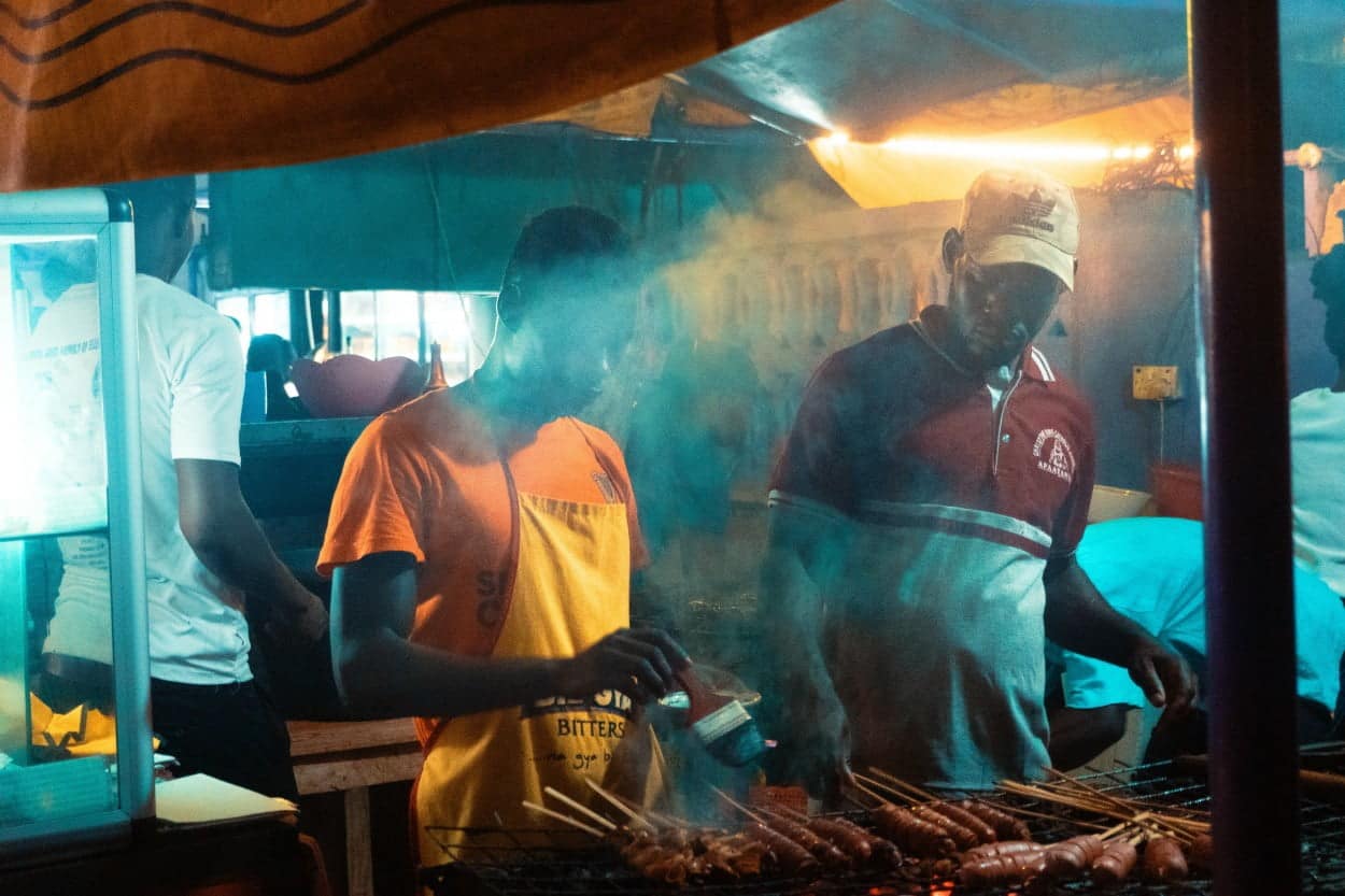 Two men cooking chichinga on an outdoor grill in Ghana.