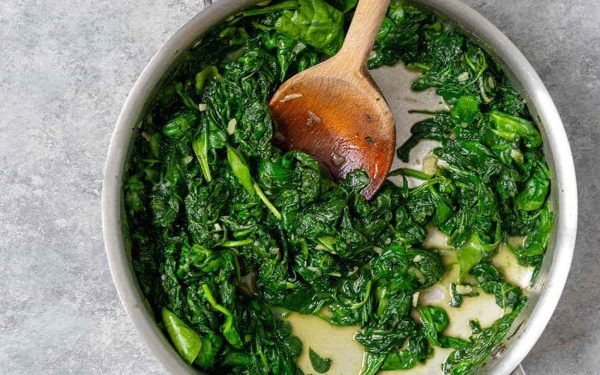 Creamed spinach with a wooden spoon in a bowl.