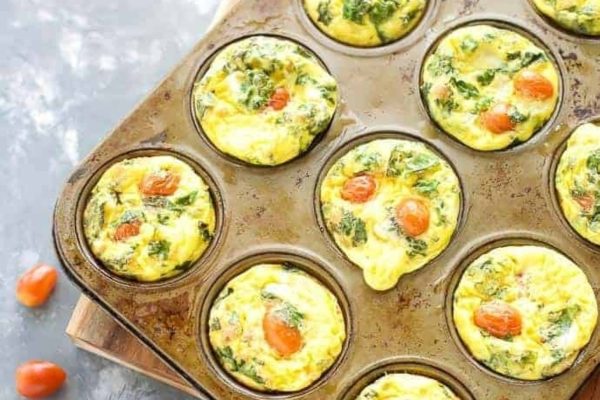 Egg muffins with spinach and tomatoes in a muffin tin.