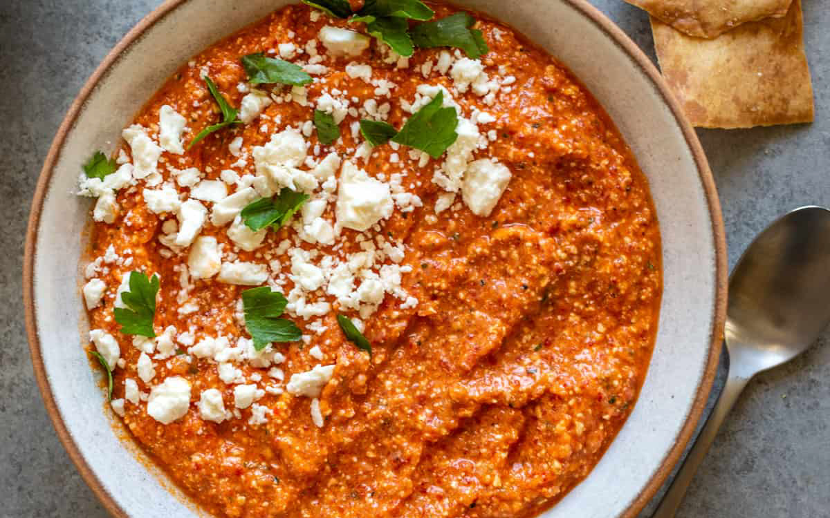 Red pepper dip with feta on top in a bowl.