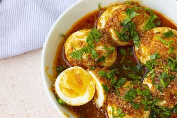 Boiled eggs in a bowl with sauce and herbs.