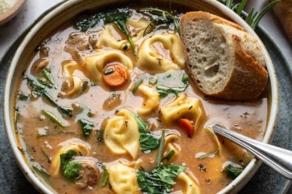 A bowl of tortellini soup with bread and spinach.