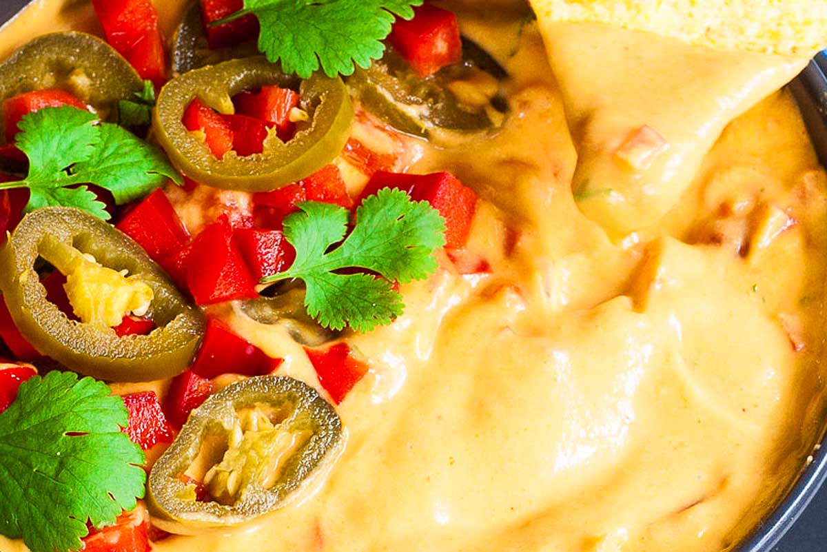 Queso dip in a bowl garnished with jalapenos and peppers.