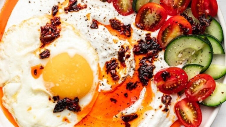 A plate with a fried egg, tomatoes and cucumbers.