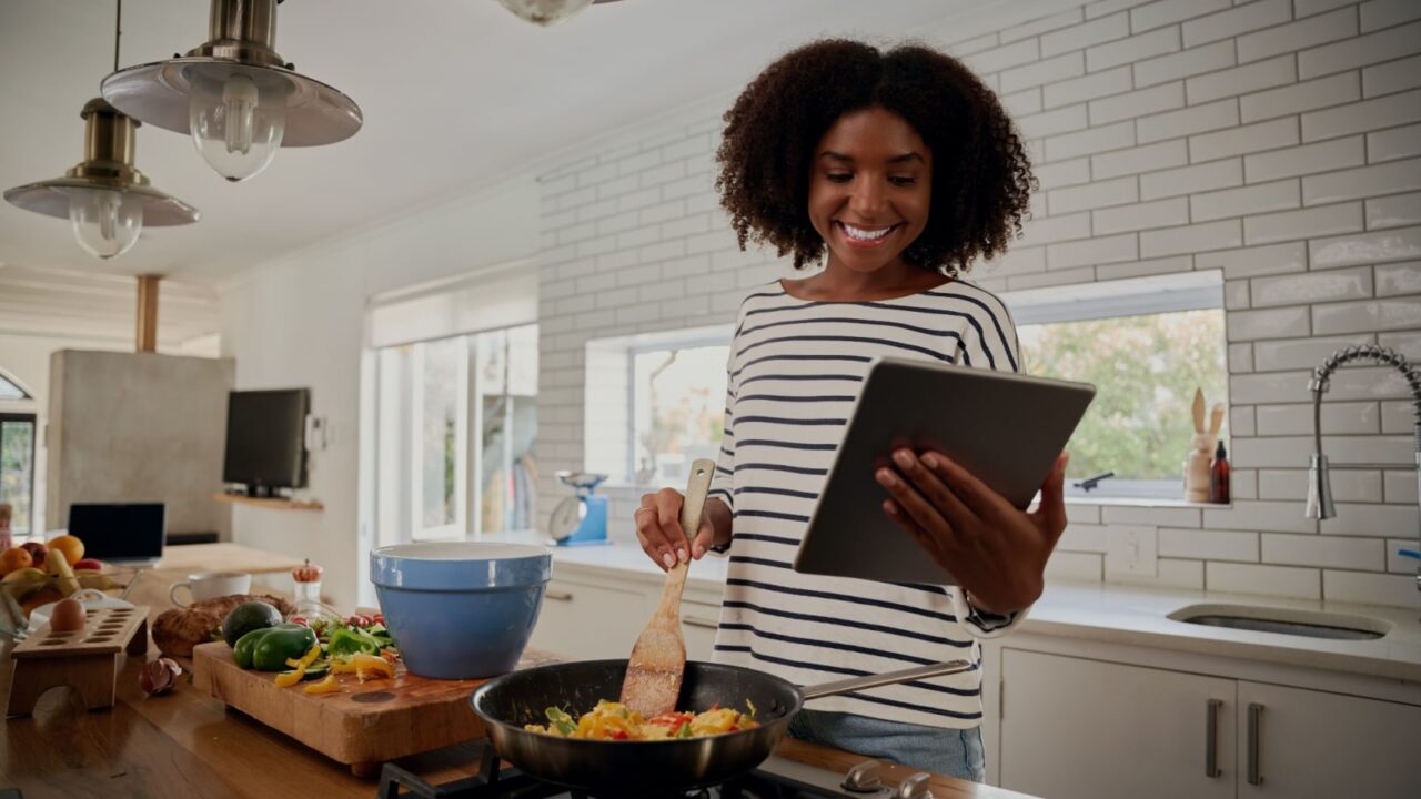 Woman looking at an ipad while cooking in the kitchen.