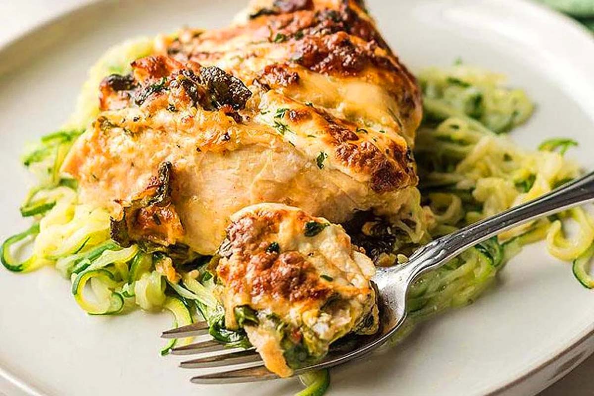 Hasselback chicken with cheese on top served with zoodles.