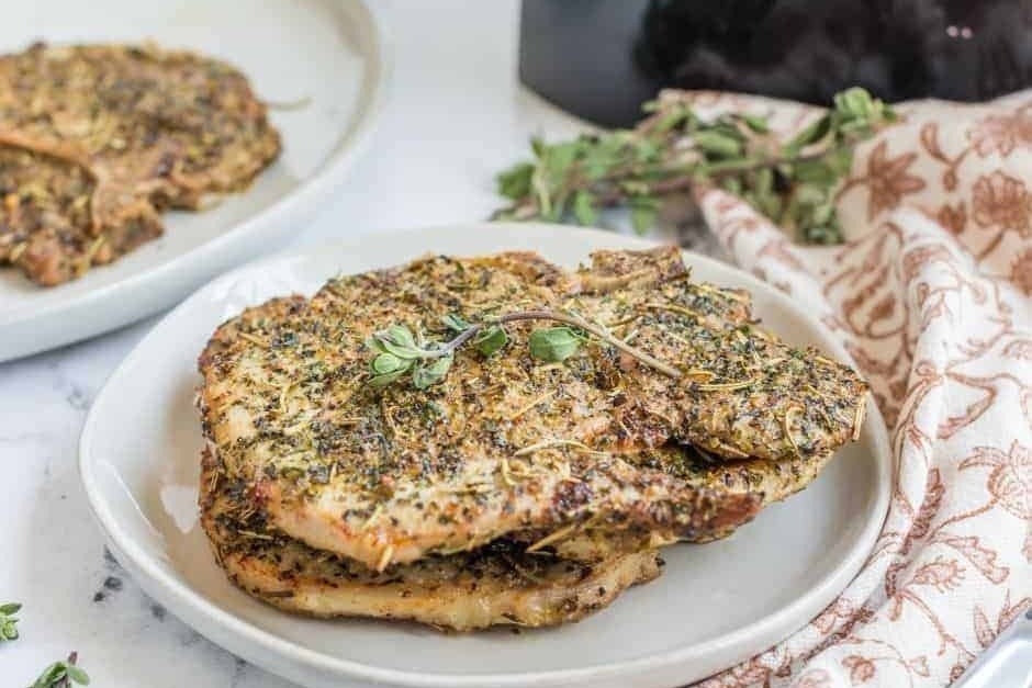 Italian pork chops topped with fresh herbs on a plate.