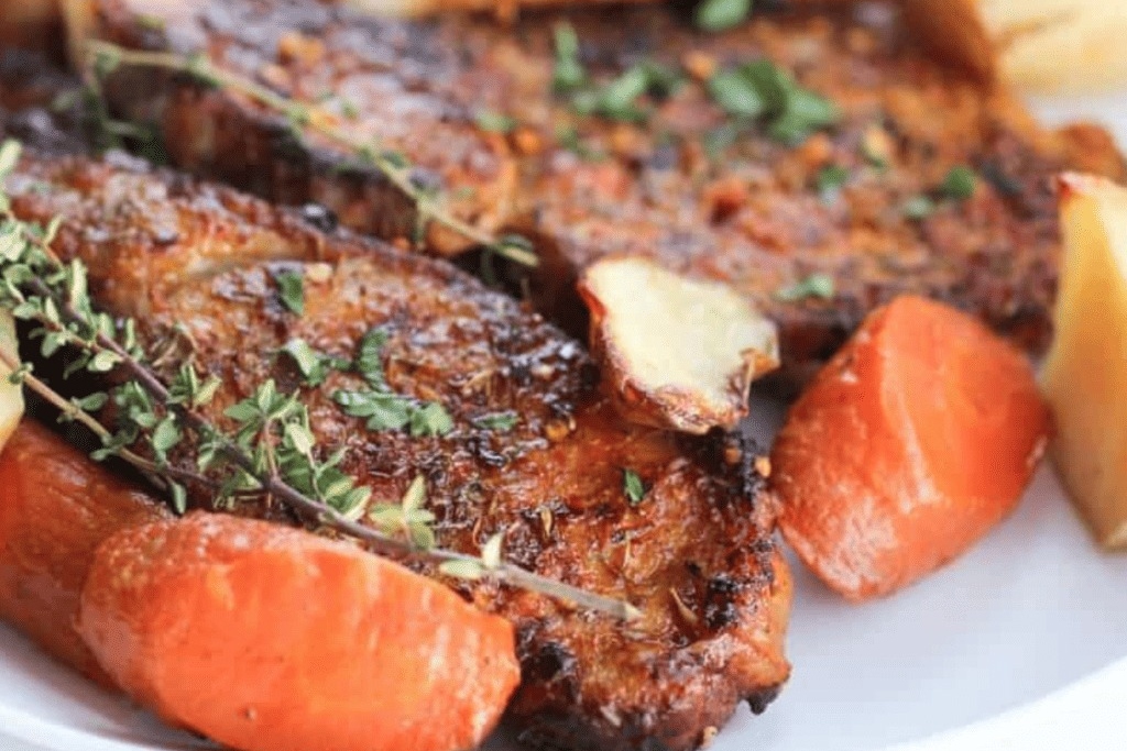 Pork chops on a plate served with carrots and fresh herbs.