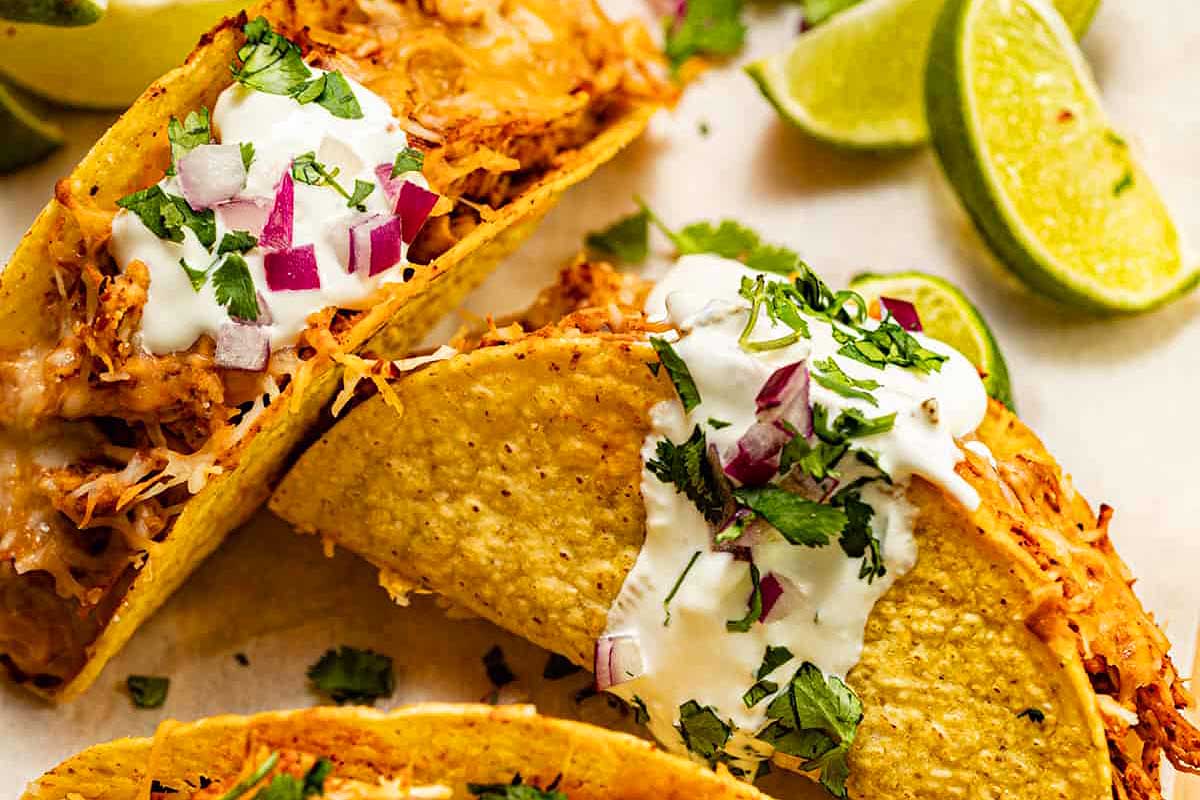 Three chicken tacos with sour cream and lime wedges.