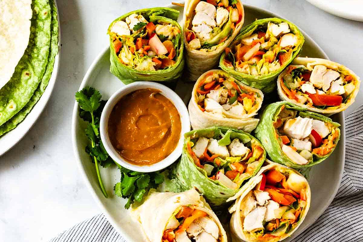 Chicken wraps with thai sauce and veggies inside of tortilla wraps.