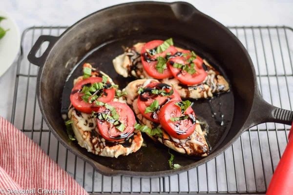 Chicken breasts in a cast iron skillet with tomatoes.