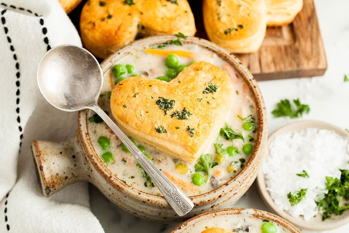 Chicken pot pie soup in a bowl with a heart shaped biscuit on top.