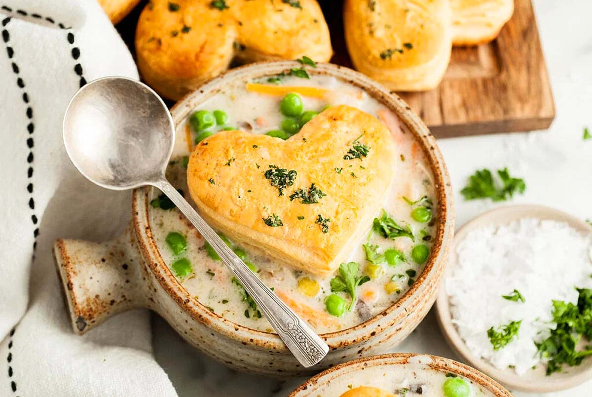 A bowl with chicken pot pie soup and a heart shaped biscuit on top.