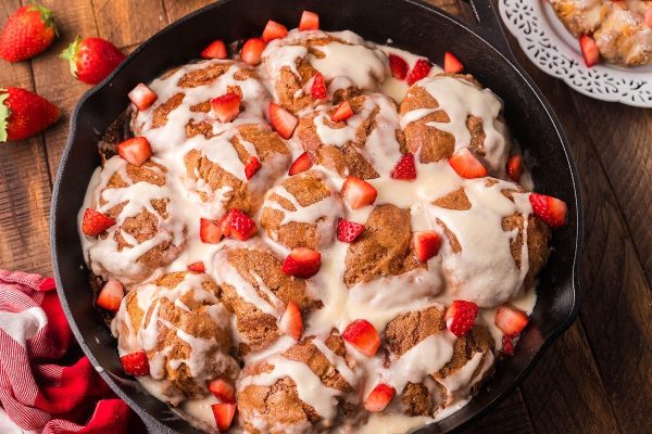 Baked cinnamon maple french toast in a skillet with strawberries on top. 