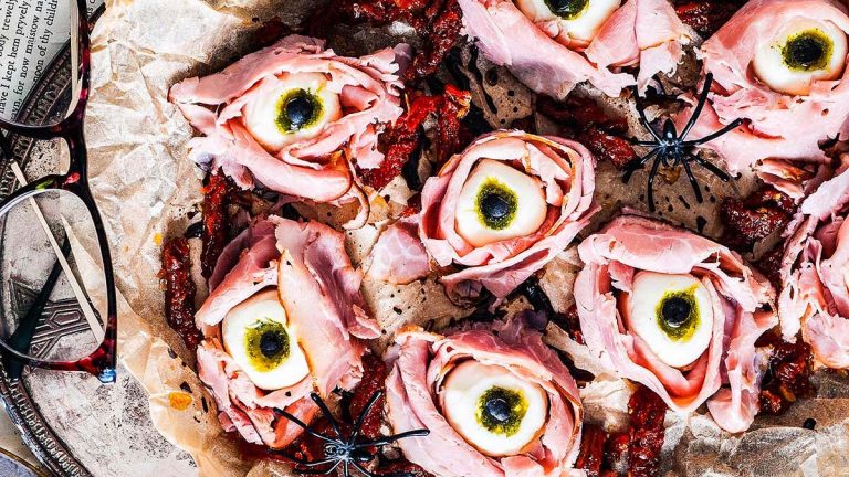 A Halloween appetizer that is eyeballs made with cheese balls, ham and olives.