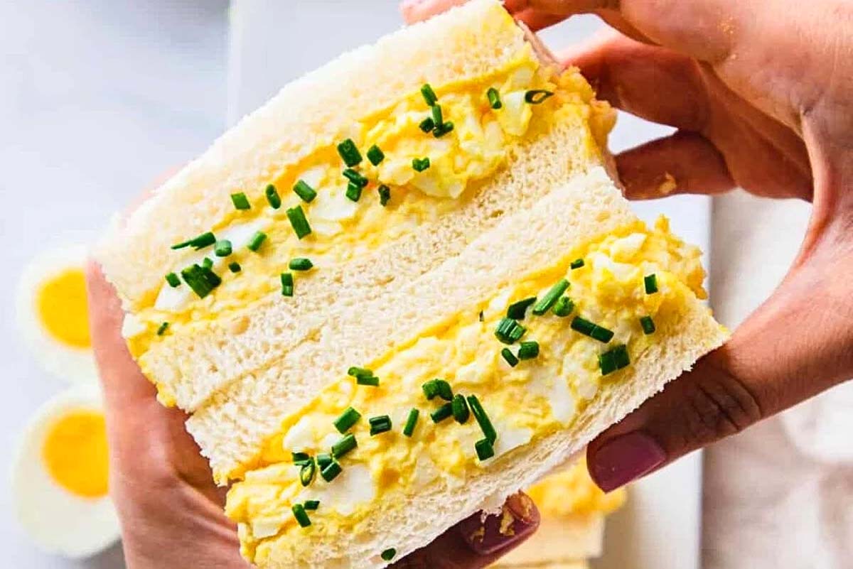 Hands holding an egg sandwich.