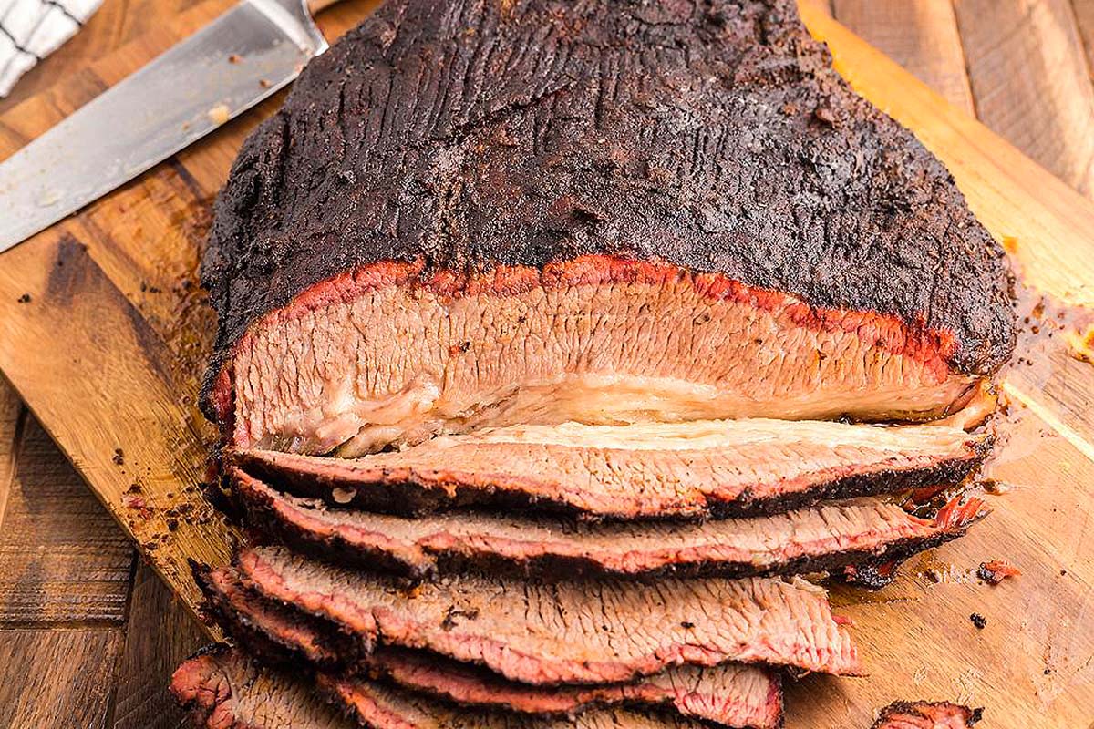 A smoked brisket being sliced on a cutting board. 