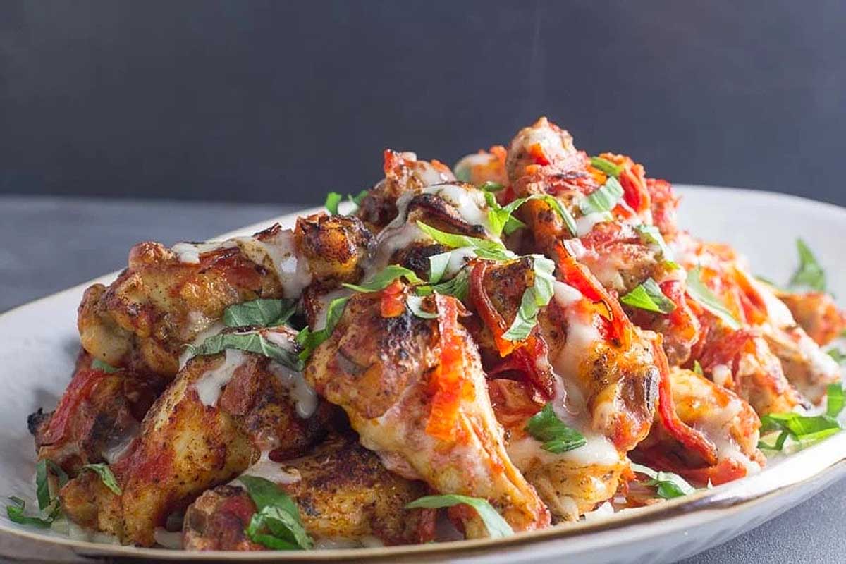 Pizza style chicken wings fusion dish with colorful garnish.