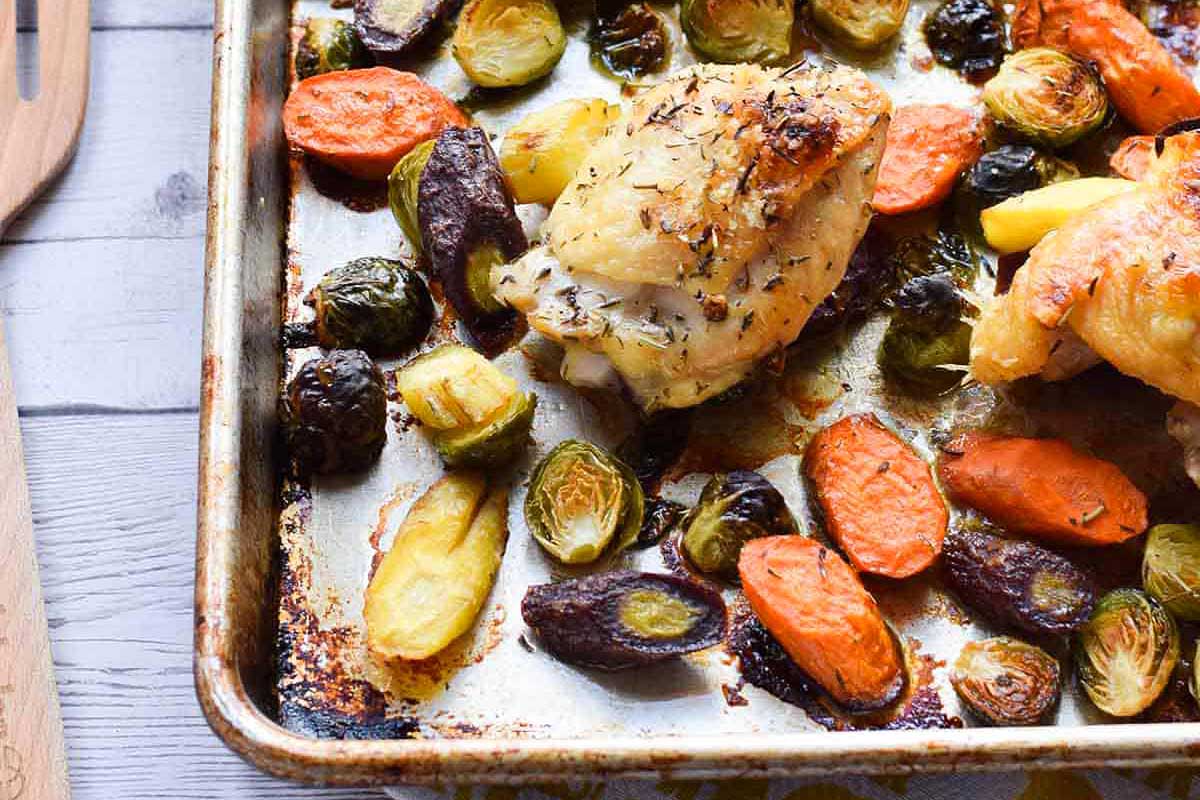 Roasted chicken with brussels sprouts and carrots on a baking sheet.