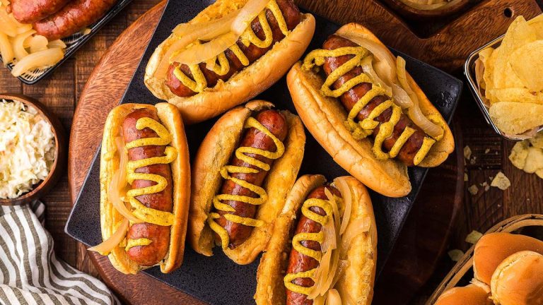 Overhead view of brats in buns and with mustard on them.