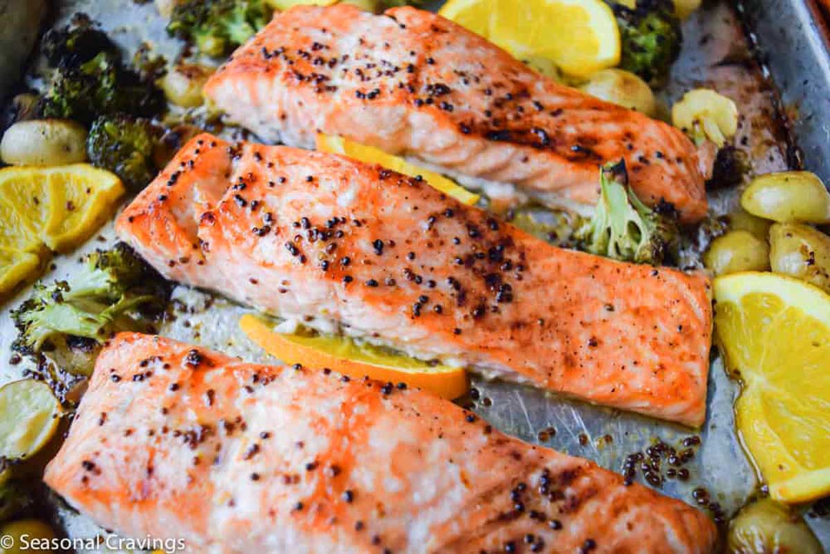 A baking sheet with salmon, broccoli and oranges.