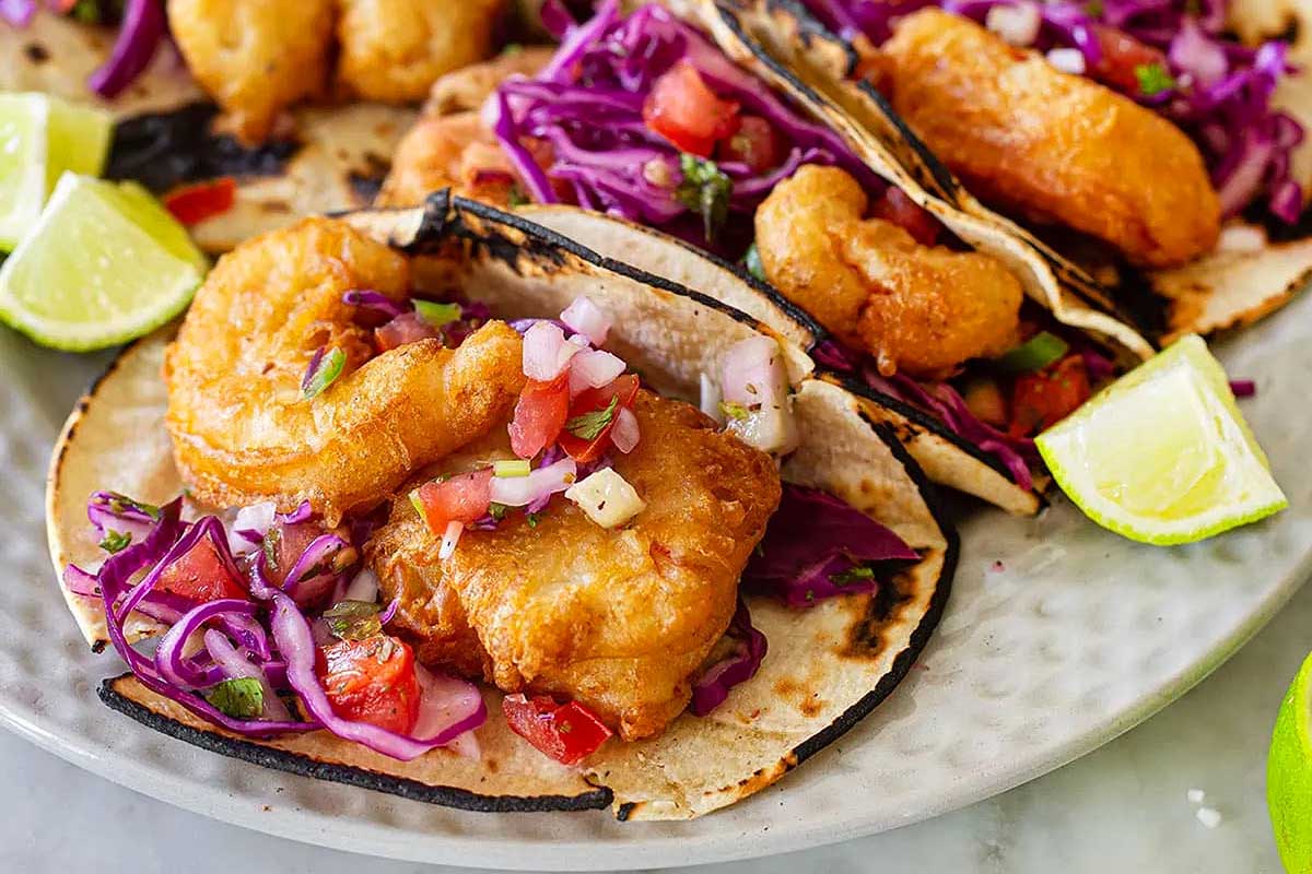 A plate of fish tacos with slaw and lime wedges.