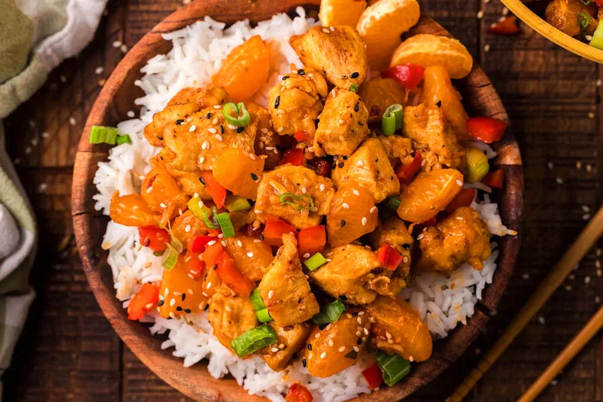 Tangerine chicken on top of white rice in a bowl.
