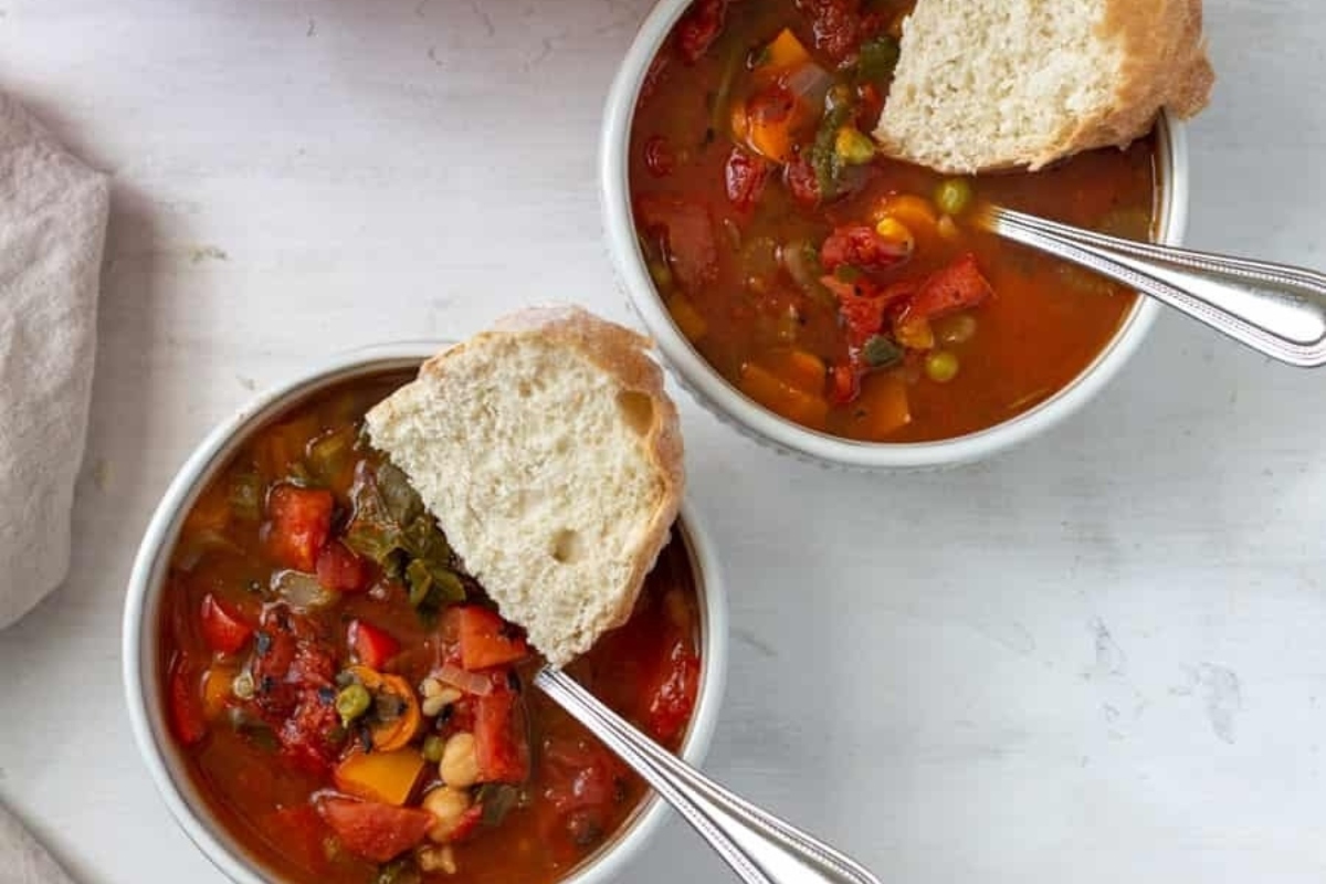 Two bowls of vegetable soup with bread.
