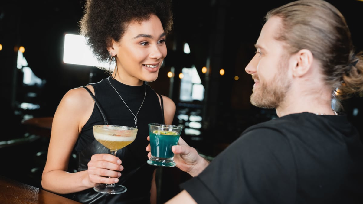 Smiling woman holding pisco sour cocktail near blurred friend in bar.