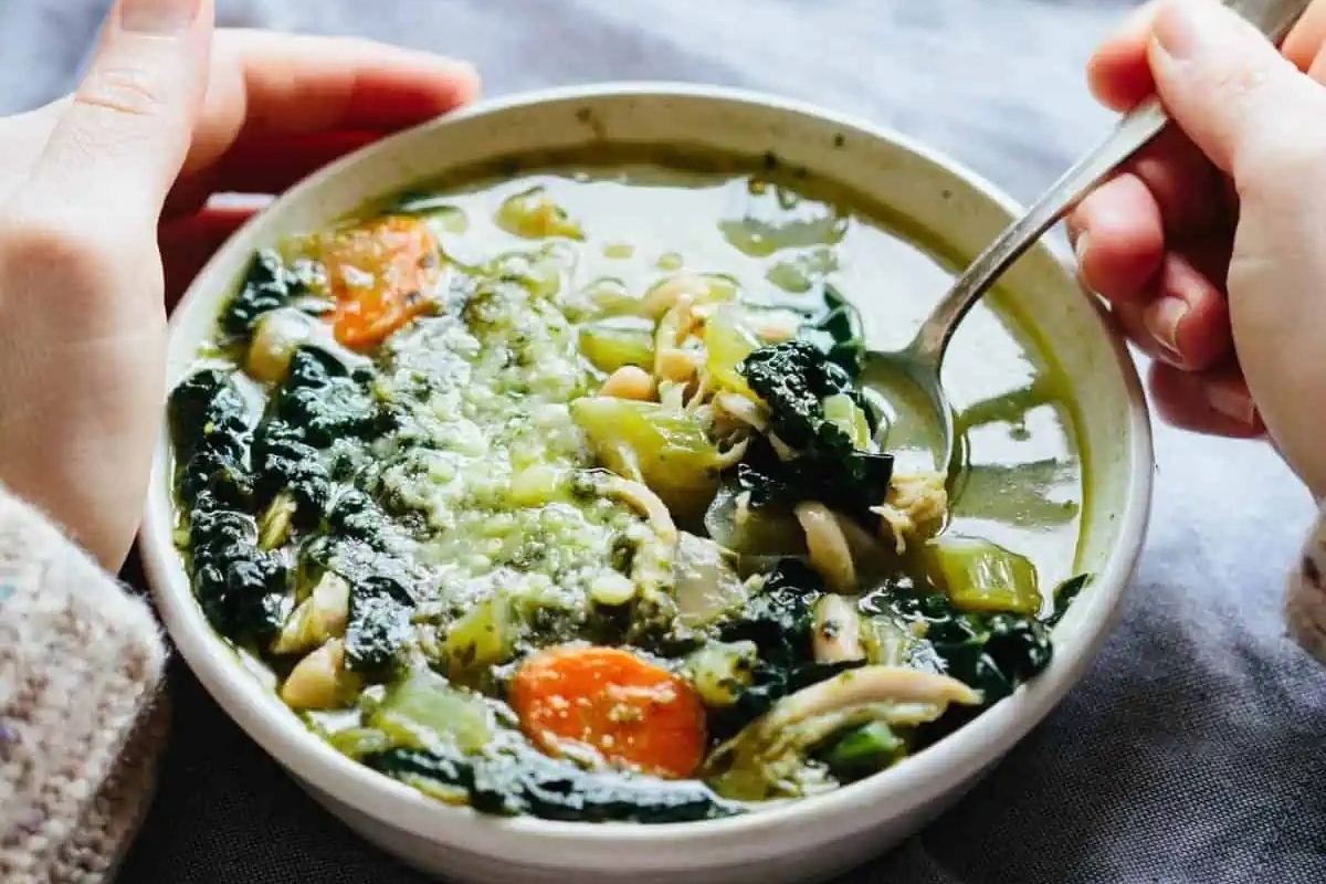 A person holding a bowl of soup featuring a delicious pesto drizzle.
