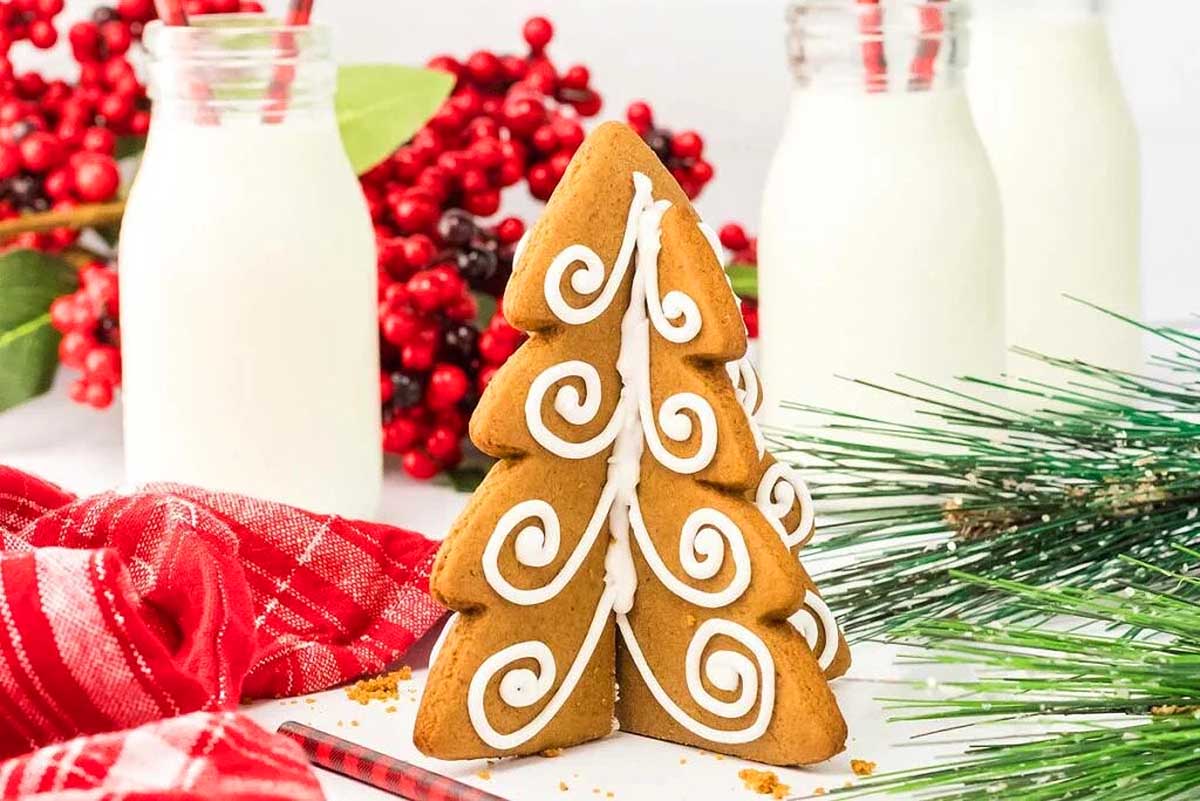 A gingerbread tree on a table next to a glass of milk.