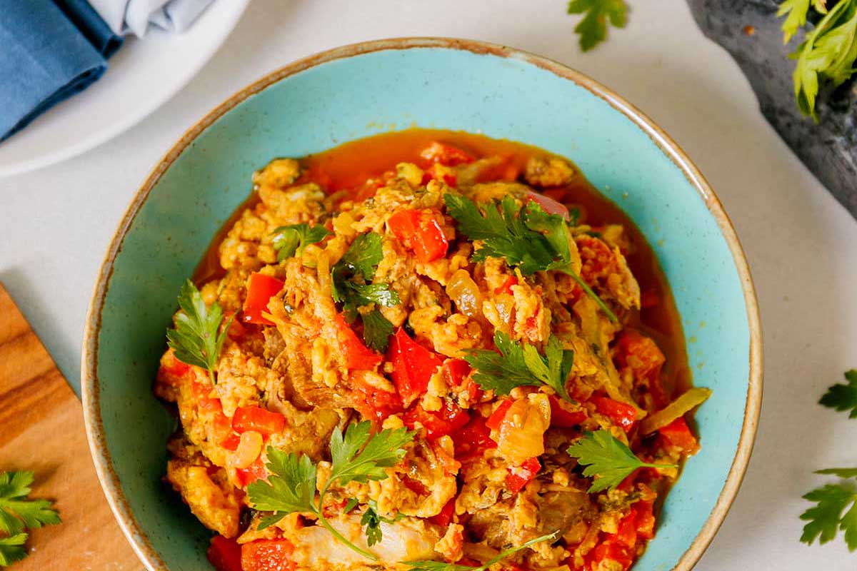A bowl of chicken curry with tomatoes and parsley.