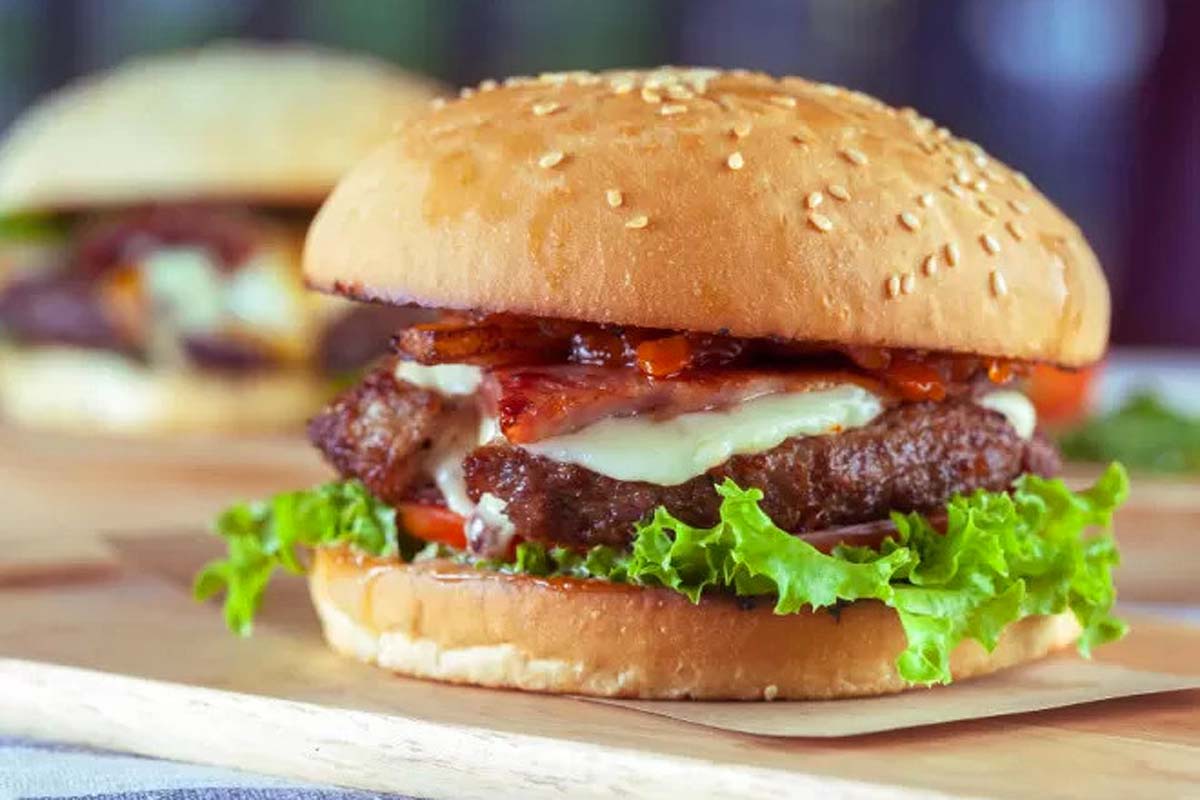 A burger with bacon and lettuce on a wooden cutting board.