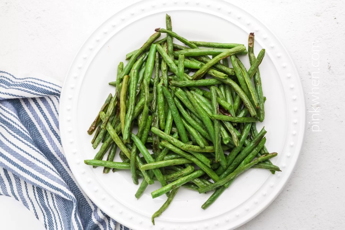 Grilled green beans on a white plate, perfect for a potluck.