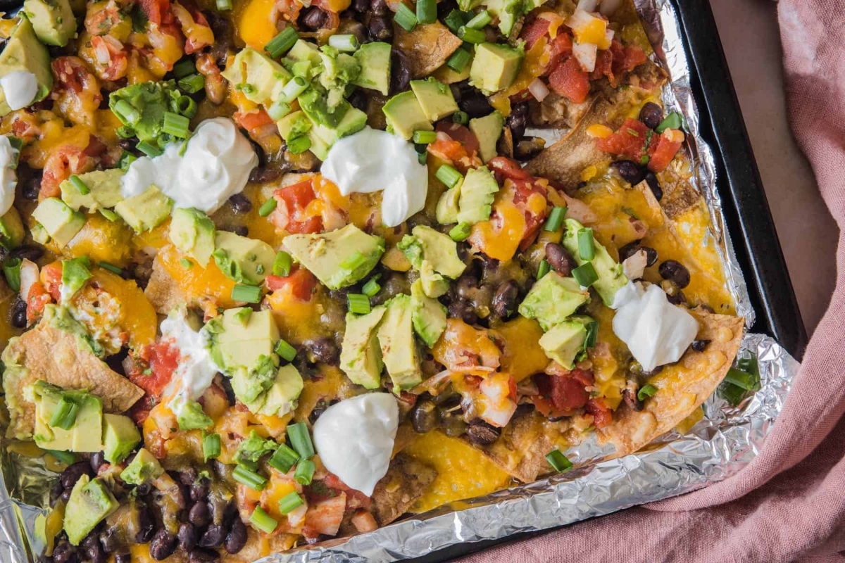 Nachos in a foil pan with avocado and sour cream.