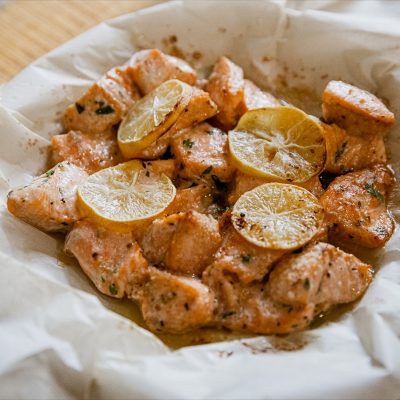 Air fryer salmon bites with lemon slices in a paper bag.
