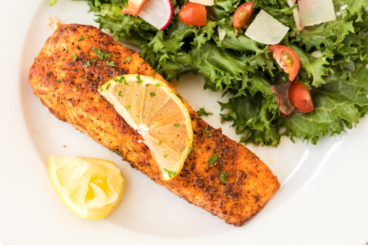 A delicious winter recipe featuring salmon cooked to perfection in an air fryer. Served on a white plate alongside a refreshing salad on the side.