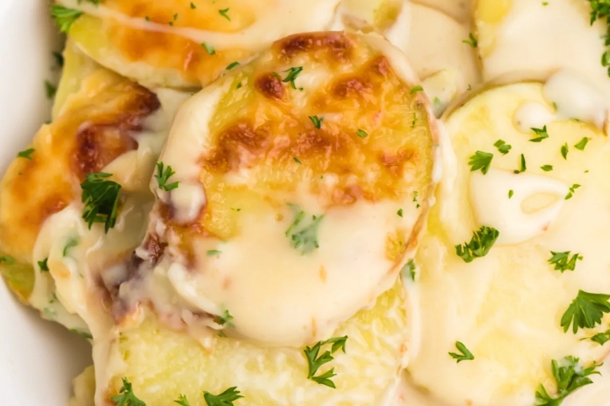 Cheap cheesy potatoes in a white bowl with parsley, perfect for a potluck or Thanksgiving.