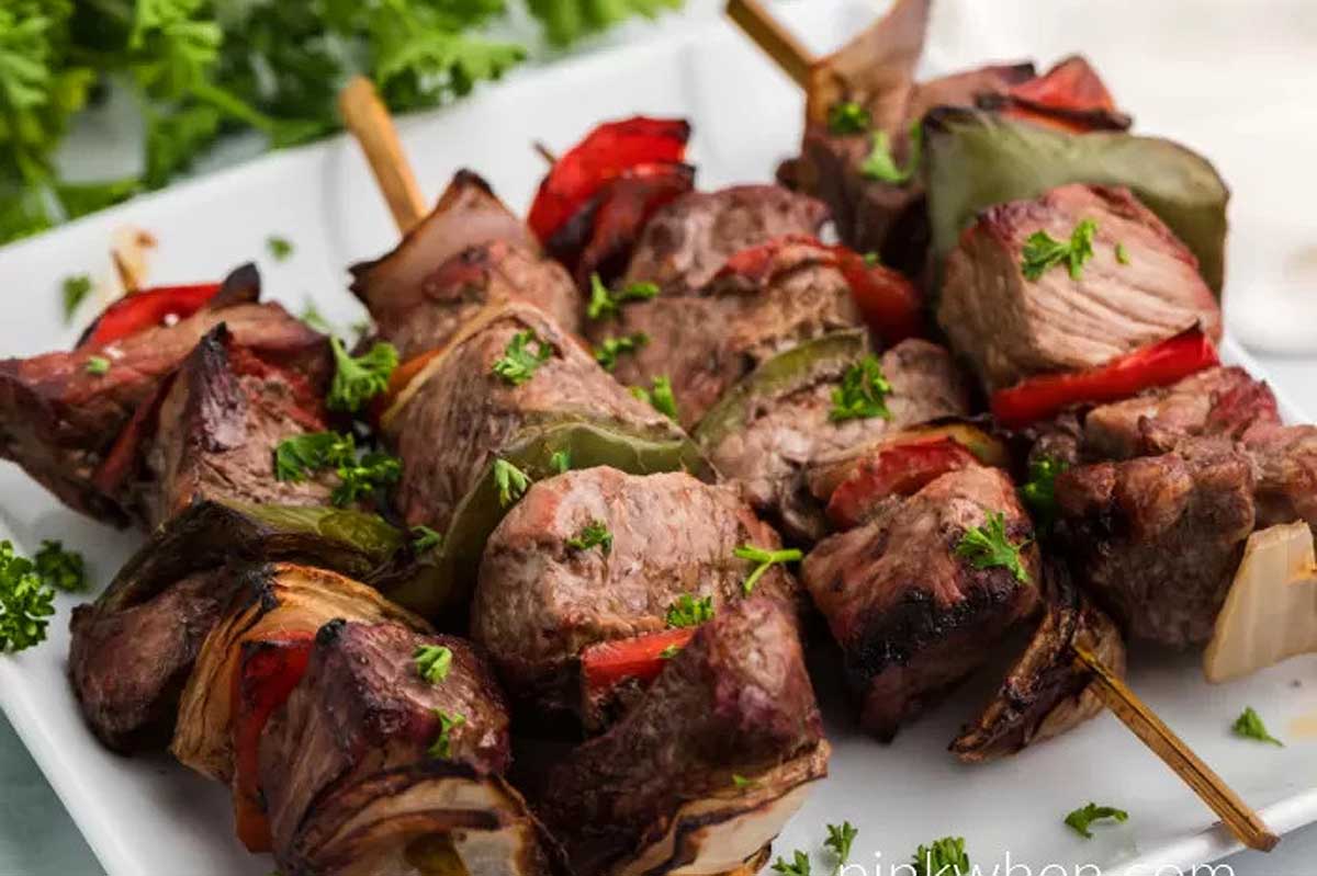 Meat skewers with peppers and herbs on a white plate.