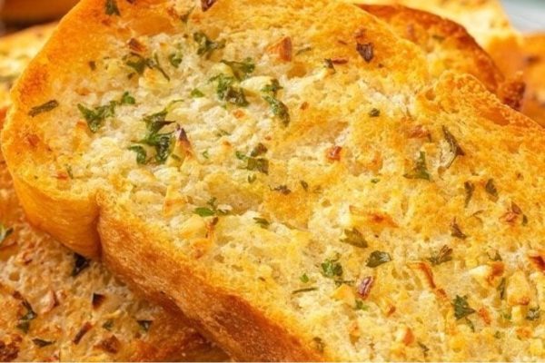 A slice of garlic bread with herbs on a plate.