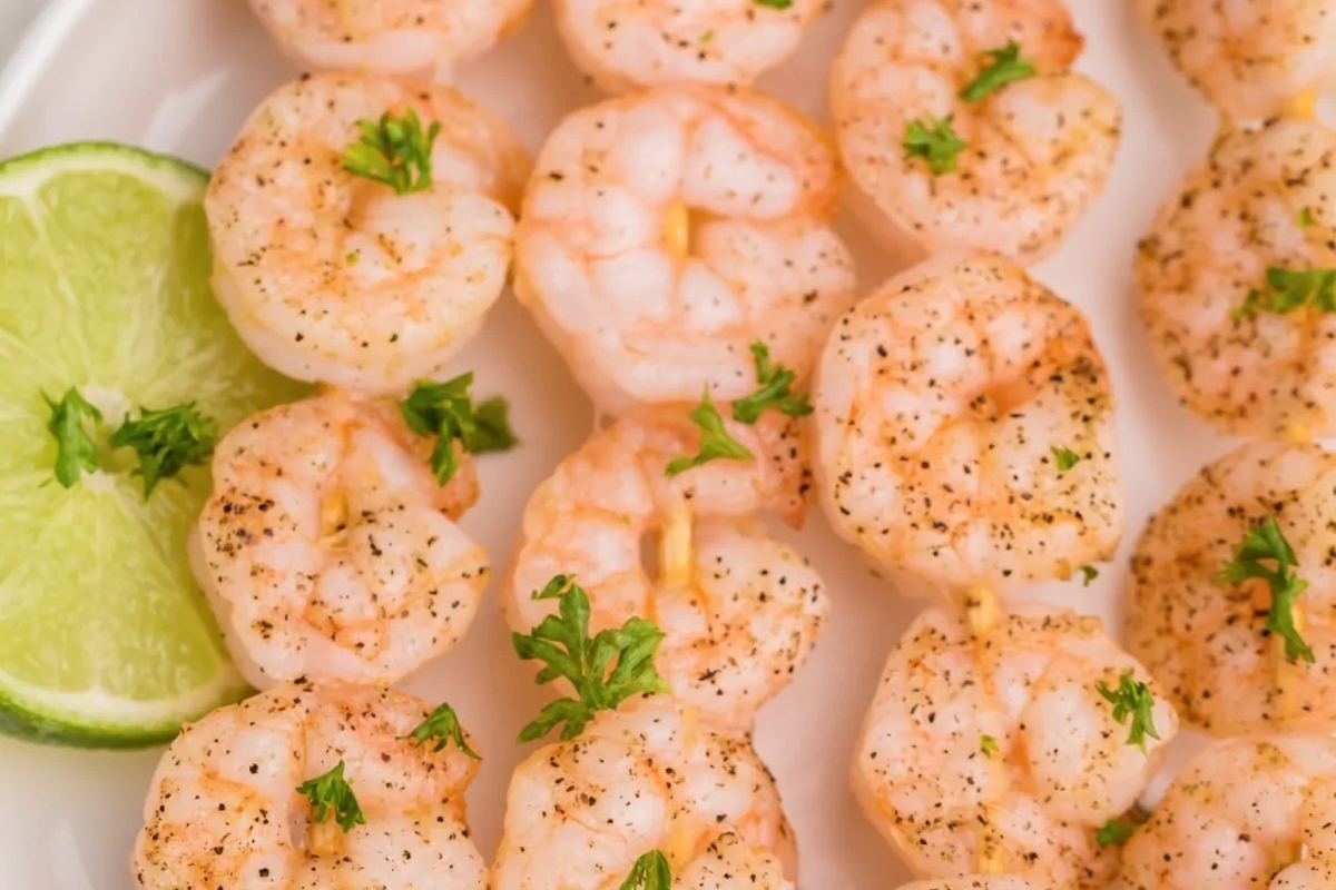 Shrimp skewers on a white plate with lime wedges.