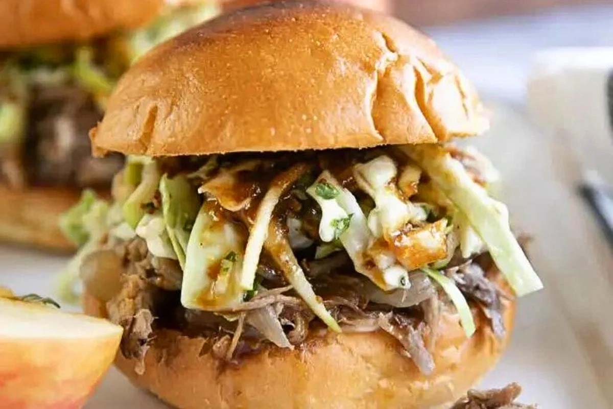 Pulled pork sliders with coleslaw on a plate, served alongside apple cider for a delightful combination of flavors.