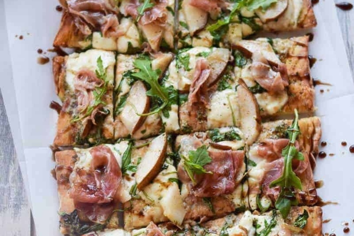 A pesto pizza with prosciutto and arugula on a white plate.